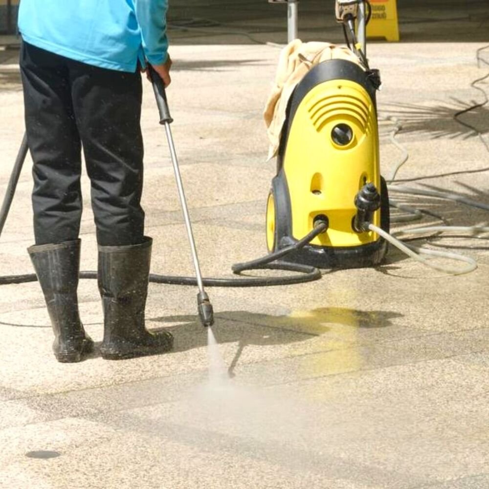 Technician power washing stained driveway beside suburban home before weekend gathering